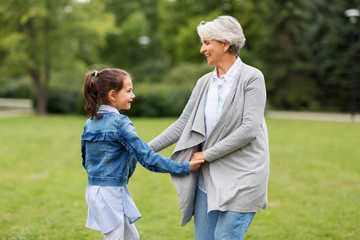 family, leisure and people concept - happy grandmother and granddaughter playing game or dancing at...