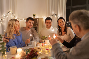 celebration, holidays and christmas concept - happy family with sparklers having fun at dinner party at home