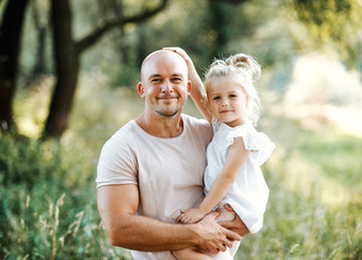 Young father in nature holding small daughter in the arms.