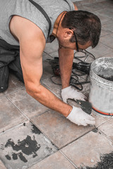 Renovation - Man construction worker laying floor tile, selective focus