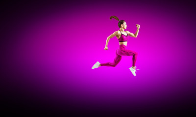 Young woman runner in purple sportswear jump in the air.