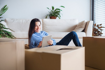 A young woman with tablet and cardboard boxes moving in a new home.