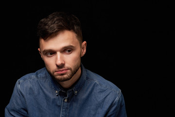 Man in denim shirt looking looking down with thoughtful