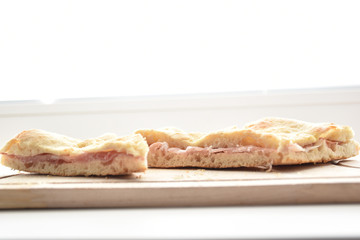 view of the pizza with ham on wooden cutting board on white background