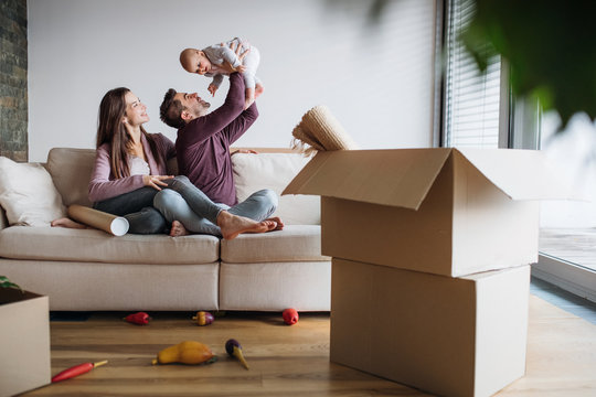 A portrait of young couple with a baby and cardboard boxes moving in a new home.