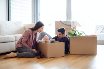 A portrait of young couple with a baby and cardboard boxes moving in a new home.