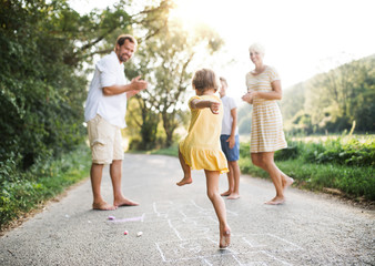 A young family with small children playing hopscotch on a road in summer.