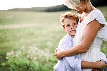 A small boy hugging his young mother outdoors in nature.