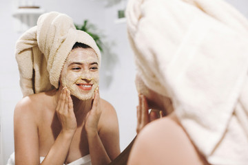 Skin Care concept. Young happy woman in towel making facial massage with organic face scrub and...