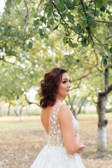 young beautiful bride walks in a summer Park with green leaves