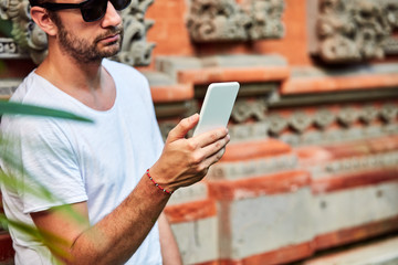 Man with sunglasses and summer shirt using smartphone.