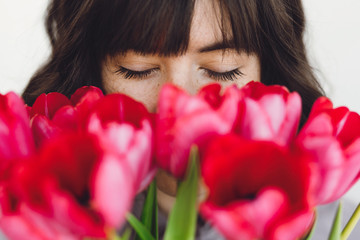 Beautiful brunette girl portrait with red tulips closeup on white background indoors, space for...