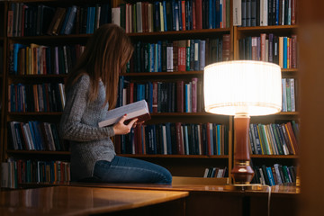 A girl reads a book in a library while sitting at a table. The girl in the library
