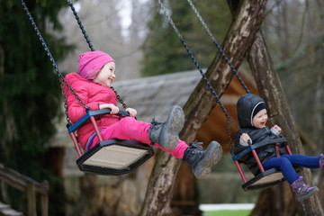 Little brother and sister laughing while having fun on a swing. Concept of freedom, carefree childhood, spending time outdoor.