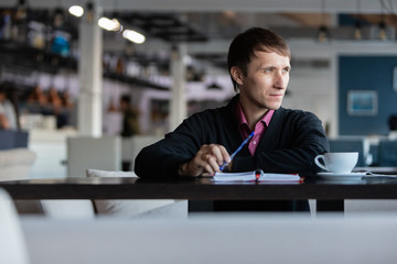 Businessman looks out the window and holds a pen in his hand. The man in the restaurant. The person thinks about matters.