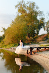 young beautiful bride and groom resting on the pier near the river at sunset