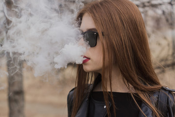 The girl in sunglasses lets out steam from the mouth. Redhead vape girl.