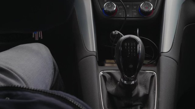 Mechanical gear shift knob, speed control during driving car near driver's foot in winter clothes at day. Bunch of keys dangling at drive. Inside of car, focus on shift lever of manual transmission