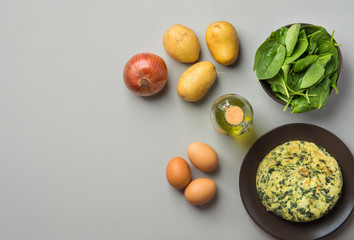 Homemade delicious potatoes eggs frittata with spinach on plate. Recipe ingredients olive oil in bottle on gray kitchen table. Overhead top view copy space. Mediterranean Latin American cuisine