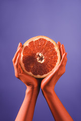 partial view of woman holding cut grapefruit in coral colored hands on blue background, color of 2019 concept