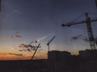 Construction site, building and crane silhouette in amazing sunset, view of city and sky. Blue and yellow sky with clouds, atmospheric scene of new construction building in evening or morning.