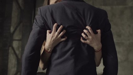 Close-up of woman's hands plugging manicured nails into man's back dressed in formal wear in night club. Midsection of passionate female flirting with confident businessman indoors.
