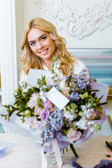 selective focus of beautiful smiling woman with flower bouquet with roses, lilac and blank card on foreground