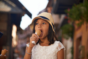 Cute Asian girl wearing a straw hat enjoying an ice cream in summer sunshine