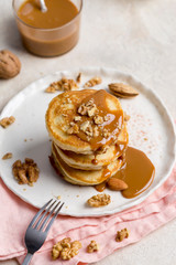 Stack of pancakes with caramel and walnuts on white plate