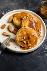 Close up fresh pancakes with caramel and nuts at white plate on dark background