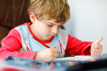 Portrait of cute happy school kid boy at home making homework. Little child writing with colorful pencils, indoors. Elementary school and education. Kid learning writing letters and numbers