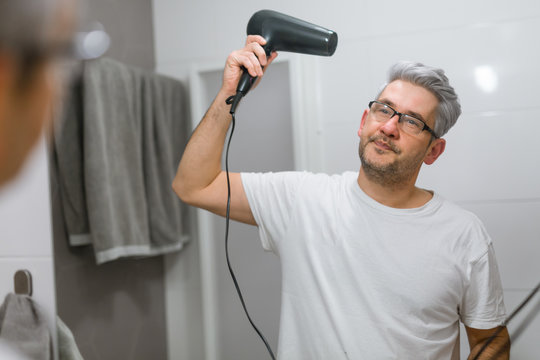 middle aged man drying hair in bathroom with hairdryer