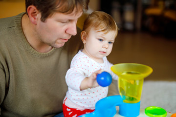 Happy proud young father having fun with baby daughter, family portrait together. Dad playing with baby girl with educational sorter toy with different colorful balls. Man with little child at home.