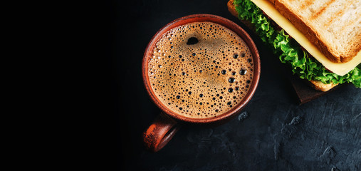 Cup with hot coffee and sandwich with grilled toast, salami sausage, salad lettuce and cheese on a dark background