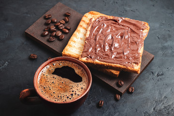 Cup with hot coffee and toast with chocolate hazelnut cream on dark background