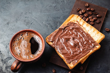 Cup with hot coffee and toast with chocolate hazelnut cream on dark background