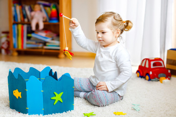Adorable cute toddler girl playing with wooden fishing game at home or nursery. Happy healthy child...