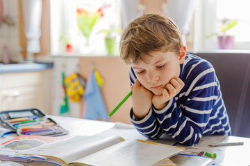 Portrait of cute happy school kid boy at home making homework. Little child writing with colorful...