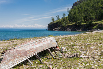 Old wooden broken inverted boat on the shore. Near a lake and rocky shore with trees. Horizontal....