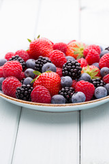 Fresh berry salad on blue dishes. Vintage wooden background.