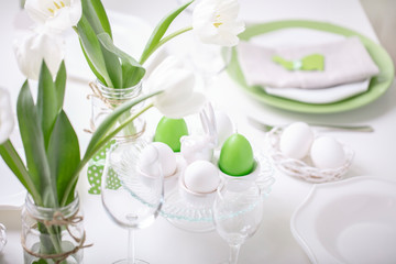 Decor and table setting of the Easter table with white tulips and dishes of green and white color. Easter decor in the form of Easter bunnies  green color with white polka dots.