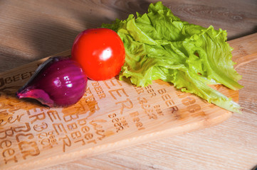 Red tomato, purple onion and green lettuce on wooden background