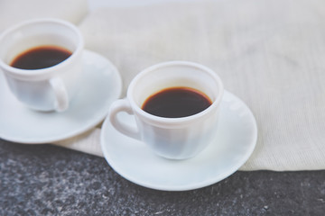 Two white cups of espresso on grey grunge background.