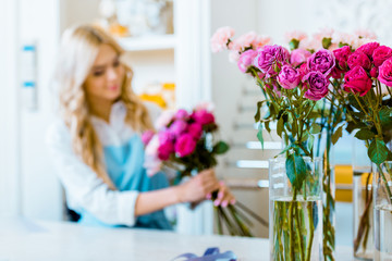 selective focus of roses with female florist arranging bouquet in flower shop on background