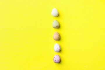 Vertical row of multicolored speckled chocolate eggs on light yellow background with linen paper texture. Easter greeting card poster banner streamer placeholder template. Minimalist