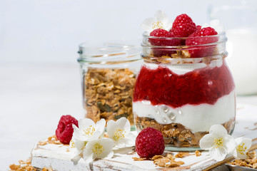 desserts with granola, and raspberries puree in jar on white wooden board