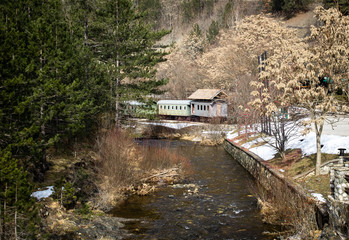 Old freight train containers with narrow gauge railway track by the mountain river. Beautiful nature, forest, stones and evergreen trees.