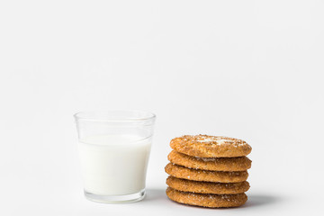 Stack of freshly home baked oatmeal and coconut cookies and glass of milk on white kitchen table background. Australian anzac biscuits recipe. Clean contemporary minimalist style. Copy space