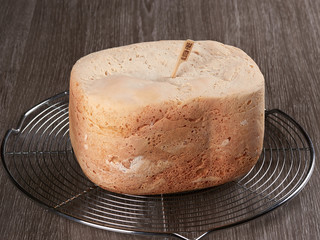Freshly baked gluten-free bread, made at home with the bread machine, set on a cooling rack, on brown background