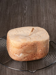 Freshly baked gluten-free bread, made at home with the bread machine, set on a cooling rack, on brown background